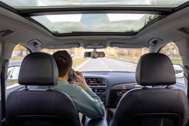 Genç bir adam araba kullanıyor. Genç bir adam araba kullanıyor ve telefonda konuşuyor. Yüksek kalite fotoğraf. Araba kullanırken direksiyonu tutan genç adam. Yolculuk. Yerel seyahat kavramı.