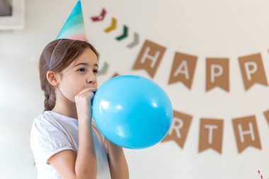 Kız bir balon şişiriyor. Doğum günü konsepti. Şişme taşaklı bir kız. Yüksek kalite fotoğraf. Arka planda mutlu yıllar..