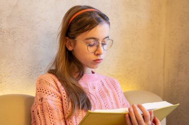 Kitap okuyan ciddi bir genç kız. Duygu konsepti. Yüksek kalite fotoğraf. Genç bir kız okul müfredatıyla ilgili bir kitap okuyor. Bir kızın yakın plan portresi..