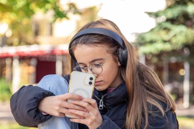 Sevimli bir genç kız telefonda fotoğraf çekiyor. Kulaklıklı kız. Yüksek kalite fotoğraf. Kulaklıklı bir kız telefonuyla fotoğraf çekiyor..