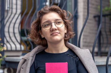 Elinde kitapla üzgün bir genç kız. Duygu konsepti. Yüksek kalite fotoğraf. Elinde kitapla gözlüklü genç bir kız. Yakın plan bir kızın hüzünlü duyguları..