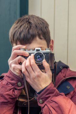 Genç bir adam eski bir kamerayla fotoğraf çekiyor. Film kamerası fotoğrafçılığı. Yüksek kalite fotoğraf. Adamın biri sokaktaki klasik bir film kamerasıyla fotoğraf çekiyor. Bir adam elinde antika bir kamera tutuyor..