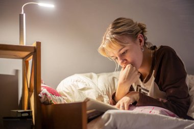 Elektrik kesintisi sırasında kitap okuyan genç bir kadın. Karanlıkta kitap okuyorsun. Yüksek kalite fotoğraf. Karartma sırasında karanlıkta kitap okuyan genç bir kadın. Güç bankasından bir el feneri parlıyor..