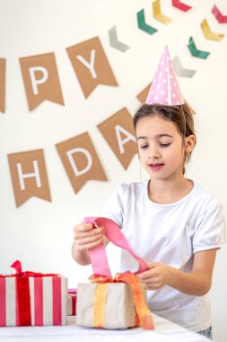Tatlı bir kız tatil hediyelerini açar. Doğum günü konsepti. Yüksek kalite fotoğraf. Renkli hediyeler. Evde doğum günü partisi. Tatil şapkalı bir kız..