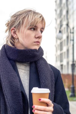 Şehirdeki üzgün genç kadın. Kadın dışarıda üşüyor. Şehirde bir yürüyüş. Yüksek kalite fotoğraf. Şehirde yürüyüp kahve içen bir kadının yakın plan portresi..