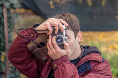 Genç bir adam eski bir kamerayla fotoğraf çekiyor. Film kamerası fotoğrafçılığı. Yüksek kalite fotoğraf. Adamın biri sokaktaki klasik bir film kamerasıyla fotoğraf çekiyor. Bir adam elinde antika bir kamera tutuyor..