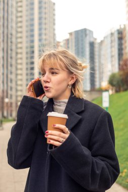 Şehirde genç ve çekici bir kadın telefonda konuşuyor. Şehirdeki kadın. Yüksek kalite fotoğraf. Sokakta elinde kahveyle gezen mutlu kız. Metin için boşluk.