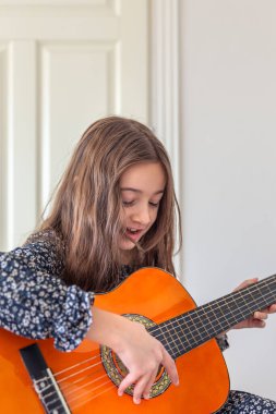 Kız evde gitar çalıyordu. Kız ve gitar. Yüksek kalite fotoğraf. Kız gitar çalıyor ve şarkılar söylüyor. Yakın plan. Yaylı bir enstrüman çalmak.