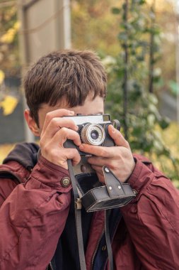 Genç bir adam eski bir kamerayla fotoğraf çekiyor. Film kamerası fotoğrafçılığı. Yüksek kalite fotoğraf. Adamın biri sokaktaki klasik bir film kamerasıyla fotoğraf çekiyor. Bir adam elinde antika bir kamera tutuyor..