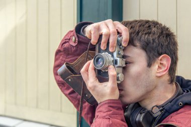 Genç bir adam eski bir kamerayla fotoğraf çekiyor. Film kamerası fotoğrafçılığı. Yüksek kalite fotoğraf. Adamın biri sokaktaki klasik bir film kamerasıyla fotoğraf çekiyor. Bir adam elinde antika bir kamera tutuyor..