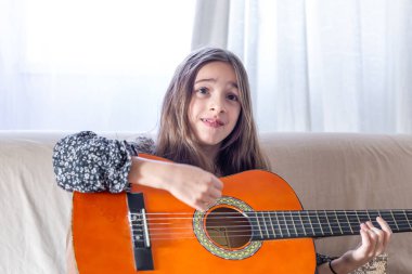Kız evde gitar çalıyordu. Kız ve gitar. Yüksek kalite fotoğraf. Kız gitar çalıyor ve şarkılar söylüyor. Yakın plan. Yaylı bir enstrüman çalmak.