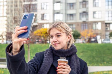 Şehirdeki genç bir kadın hatıra olarak selfie çekiyor. Şehirde güzel bir kadın. Yüksek kalite fotoğraf. Güzel kız telefonunu kullanarak selfie çekiyor..