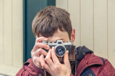 Genç bir adam eski bir kamerayla fotoğraf çekiyor. Film kamerası fotoğrafçılığı. Yüksek kalite fotoğraf. Adamın biri sokaktaki klasik bir film kamerasıyla fotoğraf çekiyor. Bir adam elinde antika bir kamera tutuyor..