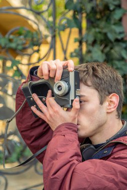 Genç bir adam eski bir kamerayla fotoğraf çekiyor. Film kamerası fotoğrafçılığı. Yüksek kalite fotoğraf. Adamın biri sokaktaki klasik bir film kamerasıyla fotoğraf çekiyor. Bir adam elinde antika bir kamera tutuyor..