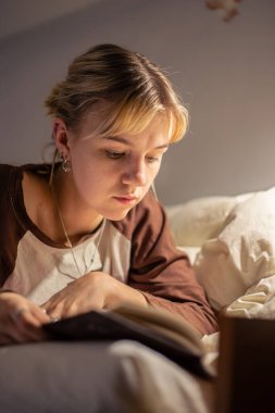 Elektrik kesintisi sırasında kitap okuyan genç bir kadın. Karanlıkta kitap okuyorsun. Yüksek kalite fotoğraf. Karartma sırasında karanlıkta kitap okuyan genç bir kadın. Güç bankasından bir el feneri parlıyor..