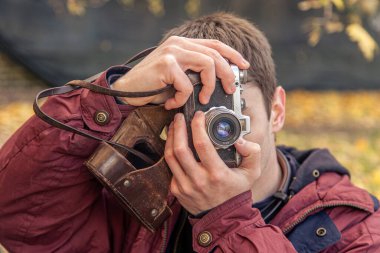 Genç bir adam eski bir kamerayla fotoğraf çekiyor. Film kamerası fotoğrafçılığı. Yüksek kalite fotoğraf. Adamın biri sokaktaki klasik bir film kamerasıyla fotoğraf çekiyor. Bir adam elinde antika bir kamera tutuyor..