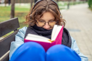 Sokakta kitap okuyan bir kız. Yakın plan. Kitap okuyan genç bir kız. Yüksek kalite fotoğraf. Gözlüklü genç ve güzel bir kadın kitap okuyor. Öğrenme kavramı.