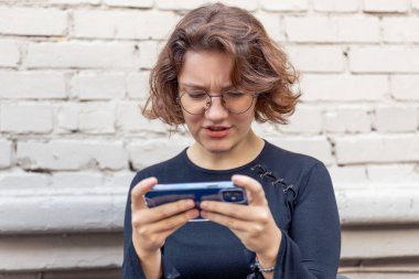 Genç bayan oyuncu bir kafede telefonda oyun oynuyor. Duygular konsepti. Yüksek kalite fotoğraf. Telefondaki oyunlar. Kız telefonda oyun oynuyor..