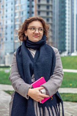 Elinde kitap olan genç bir kız öğrenci üniversiteye gider. Yüksek kalite fotoğraf. Okula dönelim. Elinde kitap tutan gözlüklü bir kız öğrenci. Öğrenim kavramı, okul, üniversite, üniversite.