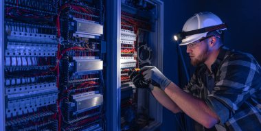 Elektrik tesisatında çalışan erkek elektrikçi. Arka planda acil durum ışıkları ve karanlık odada el feneri olan özel kıyafetli genç bir elektrik mühendisi..