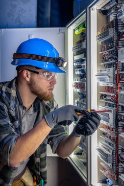 Elektrik tesisatında çalışan erkek elektrikçi. Arka planda acil durum ışıkları ve karanlık odada el feneri olan özel kıyafetli genç bir elektrik mühendisi..