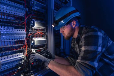 Elektrik tesisatında çalışan erkek elektrikçi. Arka planda acil durum ışıkları ve karanlık odada el feneri olan özel kıyafetli genç bir elektrik mühendisi..