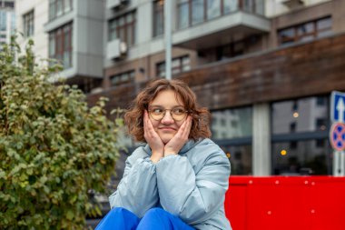 Büyük bir şehirde genç bir kadın. Şehrin tadını çıkaran bir kız. Mesaj için yer var. Yüksek kalite fotoğraf. Gözlüklü ve mavi ceketli kız. Şehirde mutlu bir kız. Kısa saçlı. Arka planda yüksek binalar var.