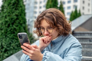 Genç bir kız şehirde telefon kullanıyor. Şehirdeki kız. Yüksek kalite fotoğraf. Teknoloji konsepti. Gadget bağımlılığı. Gözlüklü kız.