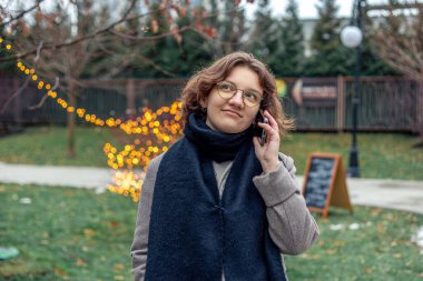 Şehirde genç bir kadın telefonda konuşuyor. Soğuk havada telefonda konuşan bir kız. Yüksek kalite fotoğraf. Gözlüklü kız.