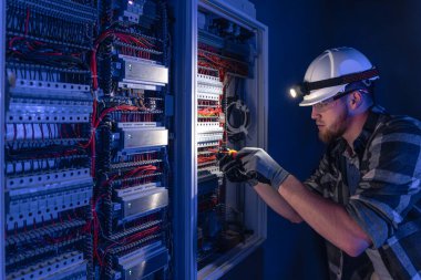 Elektrik tesisatında çalışan erkek elektrikçi. Arka planda acil durum ışıkları ve karanlık odada el feneri olan özel kıyafetli genç bir elektrik mühendisi..
