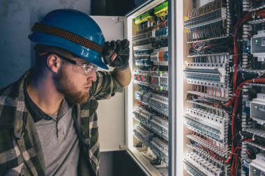 Elektrik tesisatında çalışan erkek elektrikçi. Arka planda acil durum ışıkları ve karanlık odada el feneri olan özel kıyafetli genç bir elektrik mühendisi..