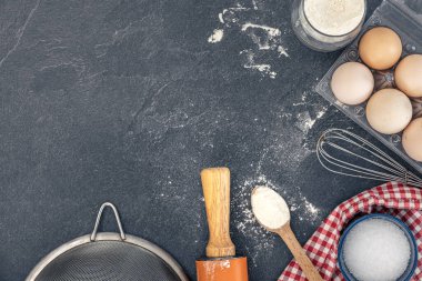 Pişirme arka planı. Kek pişirmek için gerekli malzemeler. Yumurta, un ve merdane. Yüksek kalite fotoğraf. Üst manzara, düz yatış. Uzayı kopyala Koyu bir arka planda pişirme malzemeleri. Masada un var..