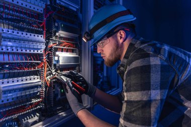 Elektrik tesisatında çalışan erkek elektrikçi. Arka planda acil durum ışıkları ve karanlık odada el feneri olan özel kıyafetli genç bir elektrik mühendisi..