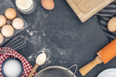 Pişirme arka planı. Kek pişirmek için gerekli malzemeler. Yumurta, un ve merdane. Yüksek kalite fotoğraf. Üst manzara, düz yatış. Uzayı kopyala Koyu bir arka planda pişirme malzemeleri. Masada un var..