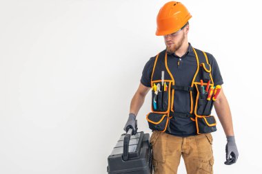 Erkek müteahhit. Tulumlu ve kasklı elektrik mühendisi alet çantasını elinde tutuyor. Hafif arkaplan. İnşaat konsepti. Mesaj için yer var. Yüksek kalite fotoğraf.