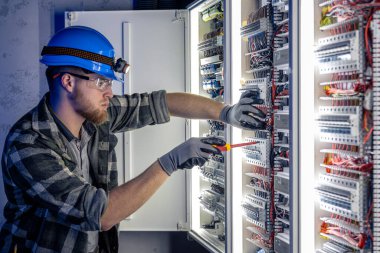 Elektrik tesisatında çalışan erkek elektrikçi. Arka planda acil durum ışıkları ve karanlık odada el feneri olan özel kıyafetli genç bir elektrik mühendisi..