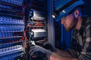 Elektrik tesisatında çalışan erkek elektrikçi. Arka planda acil durum ışıkları ve karanlık odada el feneri olan özel kıyafetli genç bir elektrik mühendisi..