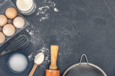 Pişirme arka planı. Kek pişirmek için gerekli malzemeler. Yumurta, un ve merdane. Yüksek kalite fotoğraf. Üst manzara, düz yatış. Uzayı kopyala Koyu bir arka planda pişirme malzemeleri. Masada un var..