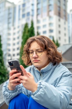 Genç bir kız şehirde telefon kullanıyor. Şehirdeki kız. Yüksek kalite fotoğraf. Teknoloji konsepti. Gadget bağımlılığı. Gözlüklü kız.