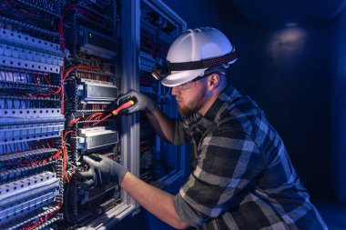 Elektrik tesisatında çalışan erkek elektrikçi. Arka planda acil durum ışıkları ve karanlık odada el feneri olan özel kıyafetli genç bir elektrik mühendisi..