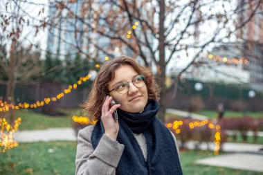 Şehirde genç bir kadın telefonda konuşuyor. Soğuk havada telefonda konuşan bir kız. Yüksek kalite fotoğraf. Gözlüklü kız.
