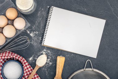 Pişirme malzemeleri ve boş kitaplarla dolu bir arka plan. Pişirme malzemeleri. Yüksek kalite fotoğraf. Uzayı kopyala Karanlık bir arka planda yemek malzemeleri. Üst manzara, düz uzanma.