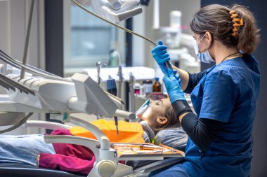 Diş muayenehanesinde genç bir dişçi. İşte bir dişçi. Diş tedavisi konsepti. Yüksek kalite fotoğraf. Çocuk dişini tedavi eden genç bir dişçi, dişçi ofisinde oturan küçük bir kız..