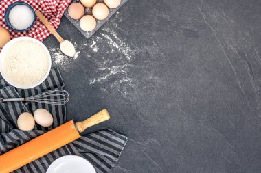 Pişirme arka planı. Kek pişirmek için gerekli malzemeler. Yumurta, un ve merdane. Yüksek kalite fotoğraf. Üst manzara, düz yatış. Uzayı kopyala Koyu bir arka planda pişirme malzemeleri. Masada un var..