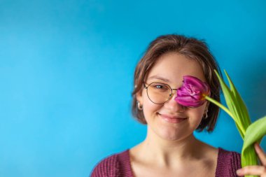 Uluslararası Kadınlar Günü. Elinde lale olan güzel bir genç kadın. Yüksek kalite fotoğraf. Mavi arka planda elinde lale olan genç bir kadın. Anneler Günü kutlaması.