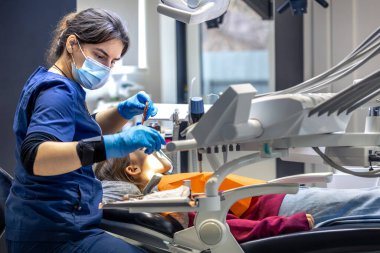 Diş muayenehanesinde genç bir dişçi. İşte bir dişçi. Diş tedavisi konsepti. Yüksek kalite fotoğraf. Çocuk dişini tedavi eden genç bir dişçi, dişçi ofisinde oturan küçük bir kız..