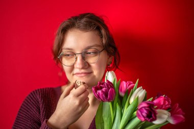 Uluslararası Kadınlar Günü. Elinde buketi olan güzel bir genç kadın. Yüksek kalite fotoğraf. Kırmızı arka planda bir buket lale olan genç bir kadın. Metin için boşluk.