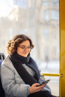 Bir kız öğrenci toplu taşımaya biniyor. Toplu taşıma ve insan konsepti. Yüksek kalite fotoğraf. Bir kız elinde telefonla toplu taşıma aracına biniyor..