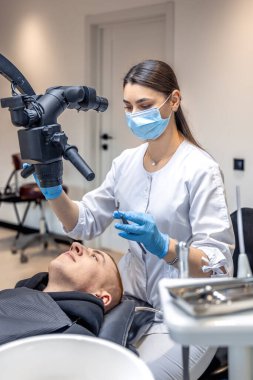 Genç bayan dişçi hastaların dişlerini diş mikroskobuyla tedavi ediyor. Dişçi konsepti. Yüksek kalite fotoğraf. Profesyonel diş tedavisi. Diş ekipmanları.