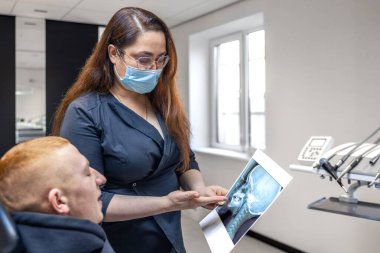 Genç bir dişçi hastaya diş röntgenini gösteriyor. Dişçi konsepti. Yüksek kalite fotoğraf. İşte bir dişçi. Dişçi ve hasta. Bir kadının yüzünde maske.